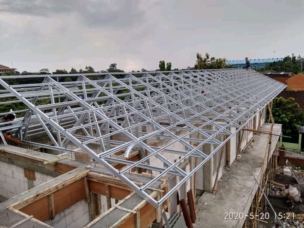 Pekerja sedang memasang rangka atap dan dinding bangunan